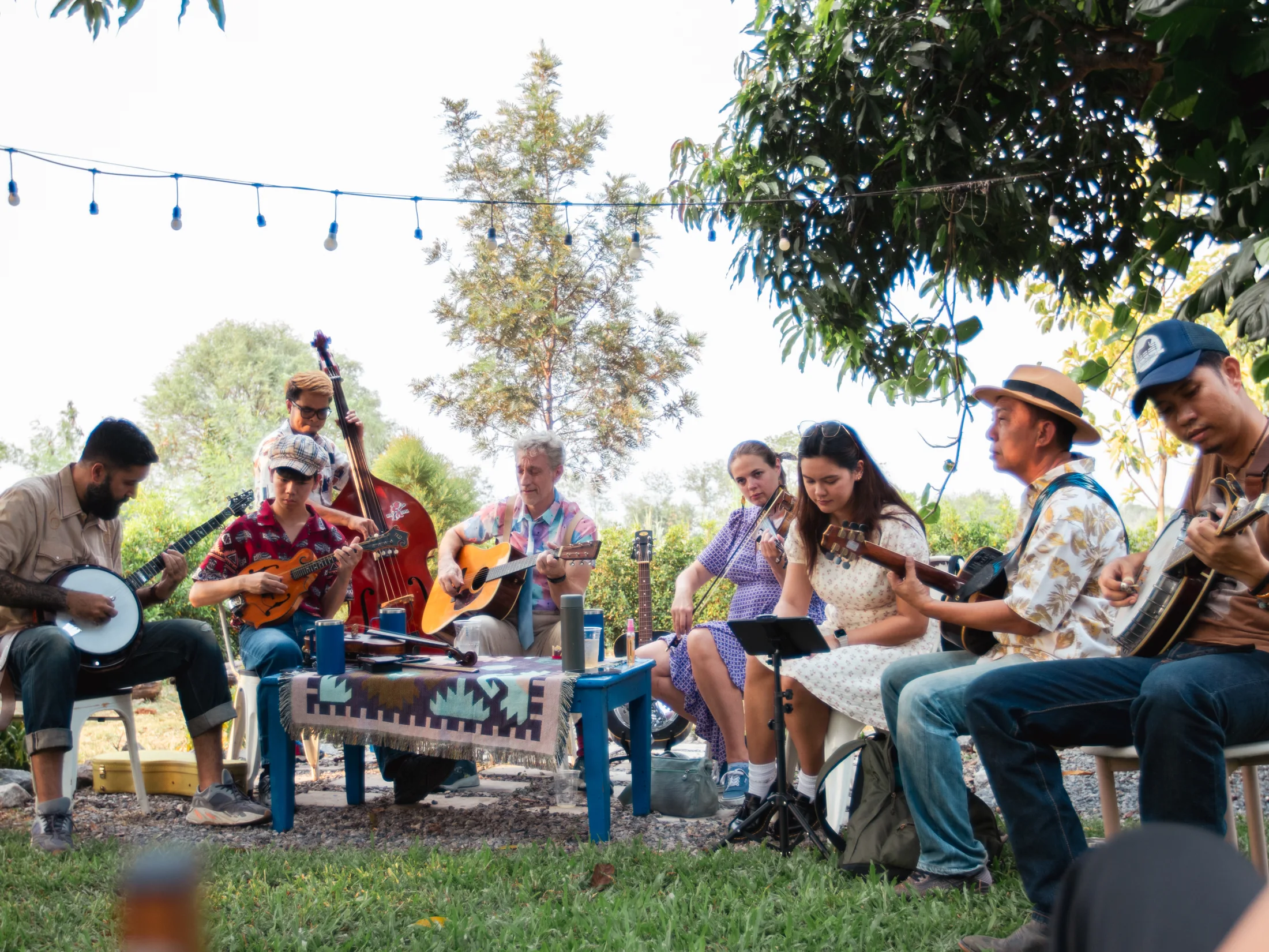 Outdoor community circle jam under trees and string lights